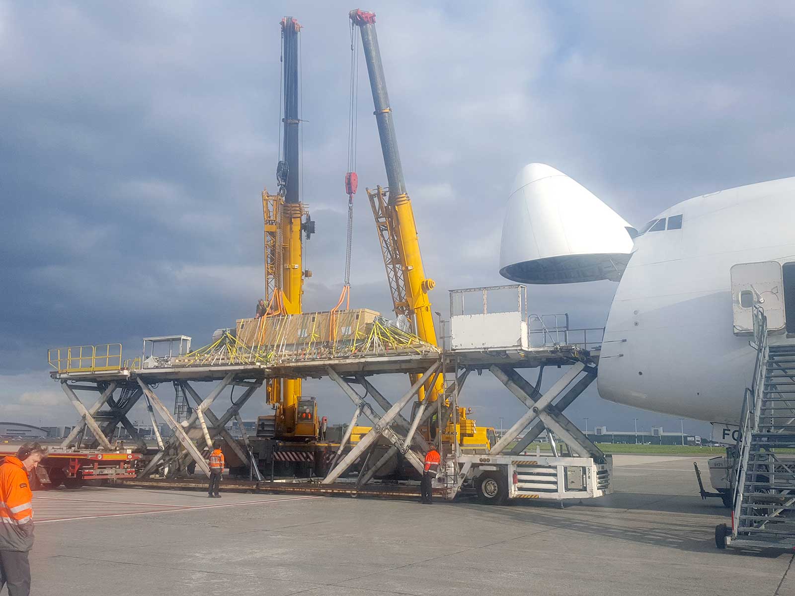 two heavy-weight cranes which just set a bulky box with very heavy content onto two high-capacity loader loading a plane from the front